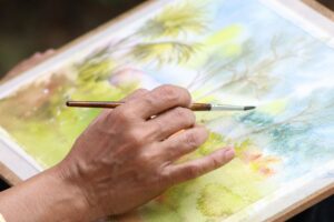 Close-up view of a hand painting a vibrant watercolor landscape. Artistic expression captured.